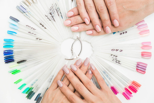 Top view of beautiful womans hands with collection of color nail polish samples on white background - Foto, Imagen