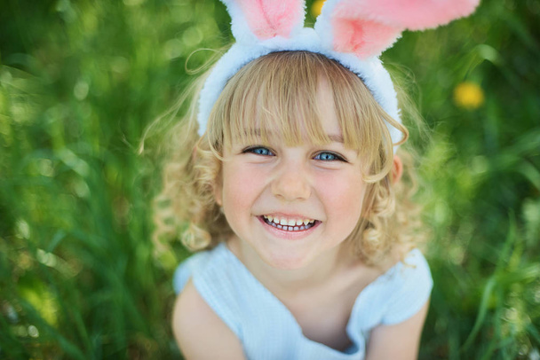 Cute funny girl with bunny ears at garden. Easter concept. Laughing child at Easter egg hunt. - Fotografie, Obrázek
