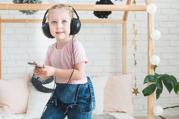 Cute little girl listening to music on headphones at home. - Foto, imagen