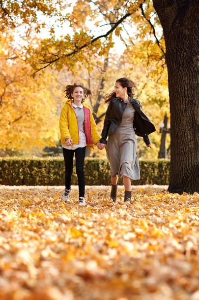 Δύο κορίτσια ευτυχισμένη τρέχει στο Φθινοπωρινό πάρκο πόλης. - Φωτογραφία, εικόνα