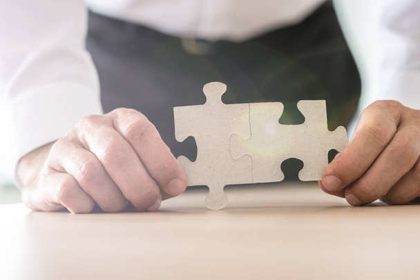 Closeup view of businessman holding two joined puzzle pieces leaning on his office desk. - Photo, Image