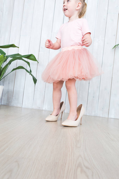 Cute little girl with her mothers shoes while standing next to plants in pots on a white background. - Foto, afbeelding
