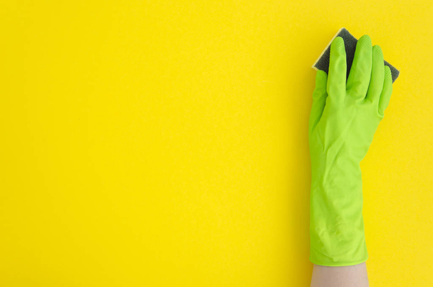 Hand in green glove with sponge on yellow background. Flat lay copy space - Zdjęcie, obraz