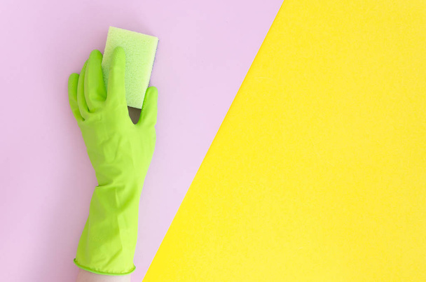 Hand in green glove with sponge on yellow pink bright split color background. Flat lay copy space vibrant duotone background - Photo, Image