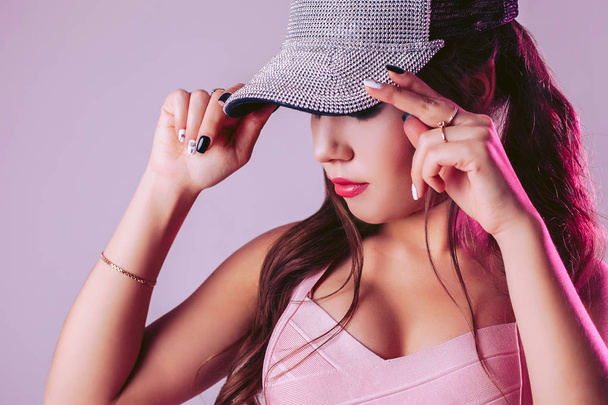Stunning woman on a light purple background in the studio, adjusts the cap on her head - Foto, Imagem