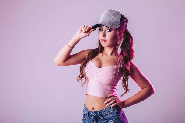 Young girl on a light purple background in the studio, adjusts the cap on her head - Фото, изображение