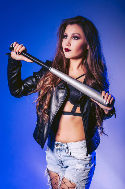 A woman in a leather jacket is holding a baseball bat. Shooting in the studio - 写真・画像