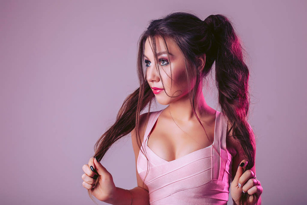 A glamorous woman on a pink-purple background holds her hair with her hands - Fotografie, Obrázek