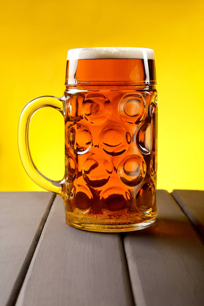 A glass, a mug of beer on a wooden table and an yellow background - Фото, изображение