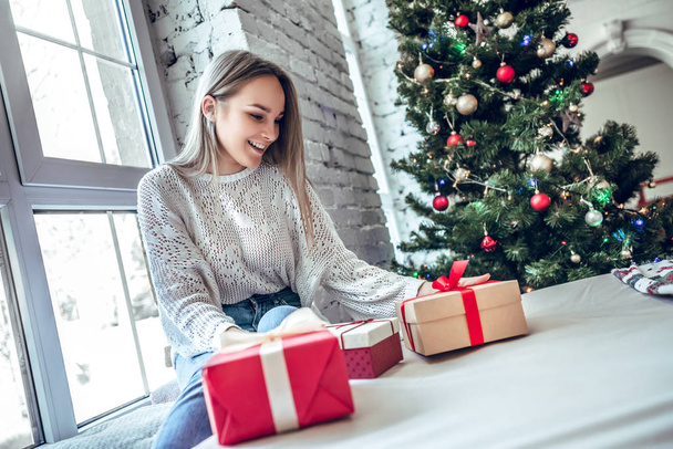 Christmas, x-mas, winter, happiness concept - smiling woman with many gift boxes. Girl opens a gift against the background of the Christmas tree. happy young woman celebrating Christmas - Фото, изображение