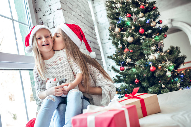 Mom and daughter dressed as Santa celebrate Christmas. Family at the Christmas tree. Woman and girl celebrate new year - Фото, изображение