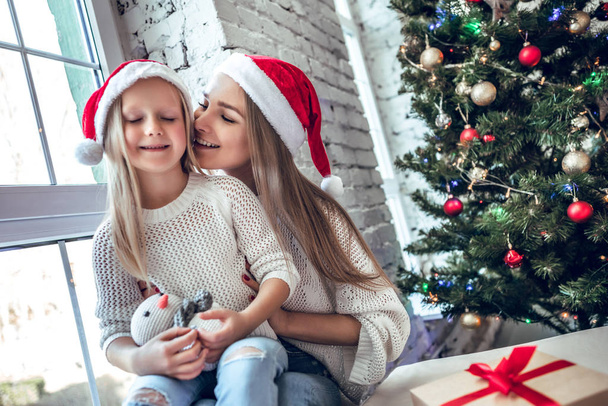 Happy family mother and child girl in santa hat near a Christmas tree with Christmas present - Foto, Bild