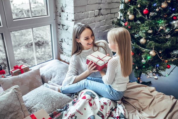 Merry Christmas and Happy Holidays! Cheerful mom and her cute daughter girl exchanging gifts. Parent and little child having fun near Christmas tree indoors. Top view - Valokuva, kuva