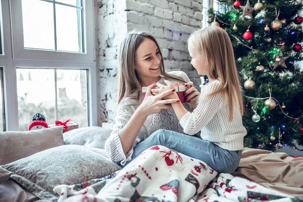 holidays, presents, christmas, x-mas, birthday concept - happy mother and child girl with gift box near Xmas tree. Morning Xmas - Fotoğraf, Görsel