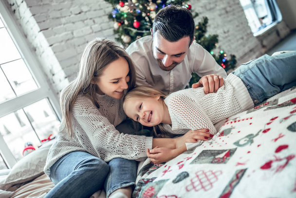 Happy family portrait of mother and girl child laying on cosy bed in festively decorated room with Christmas tree. New Year s celebration. - Foto, imagen
