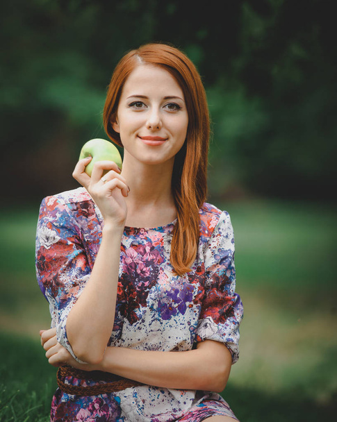 redhead girl with apple on green lawn in a park. - Foto, afbeelding