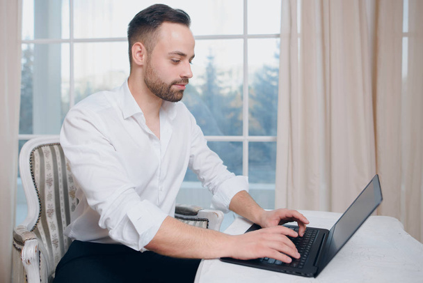 Hipster businessman typing at laptop on window background - 写真・画像