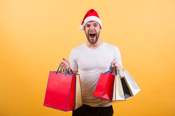 The morning before Xmas. delivery christmas gifts. man in santa hat hold christmas present. online christmas shopping. Happy new year. happy santa man on yellow background. Christmas fun. shoping bag - Photo, image