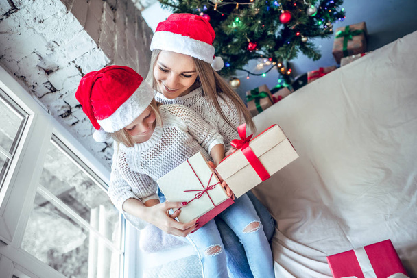 A little girl with her mom opens a New Year's gift near a festive Christmas tree. top view - Фото, изображение