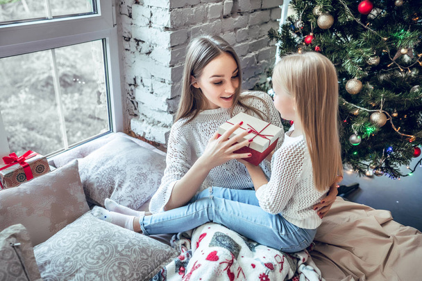 holidays and family concept - happy mother and daughter with gift box over room with christmas tree background. top view - Foto, Bild
