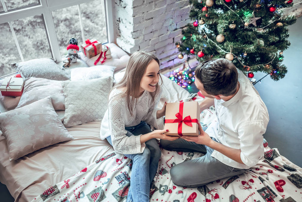 Couple in love sitting on bed near decorated Christmas tree, exchanging Christmas presents and having fun. top view - Photo, image