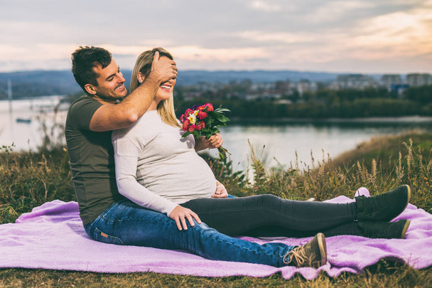 Husband giving flowers to his pregnant wife while  enjoy spending time together outdoor.Toned image. - Foto, afbeelding