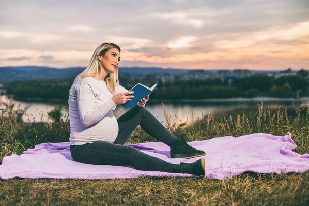 Beautiful pregnant woman enjoys reading book outdoor.Toned image. - Foto, imagen