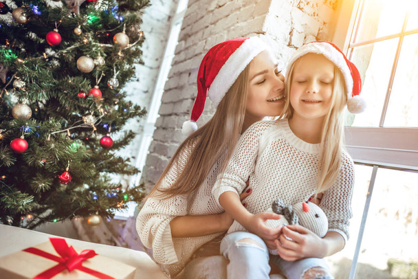 Happy family mother and child girl in santa hat near a Christmas tree with Christmas present - 写真・画像