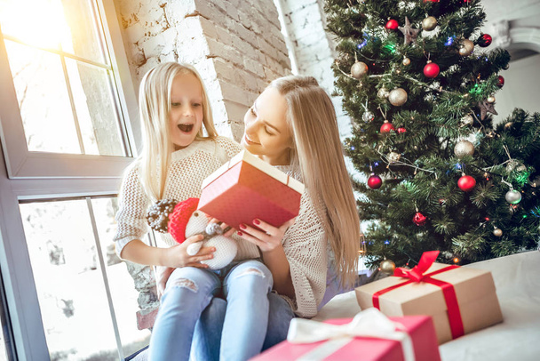 Cheerful happy woman with daughter sitting on the floor in the living room near christmas tree. New Year's interior - Foto, Bild