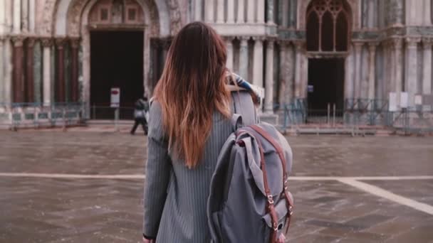 Beautiful woman tourist with backpack walking to amazing old antique building in Venice, Italy, looking back slow motion - Filmagem, Vídeo