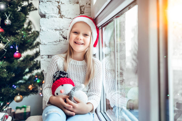 A little child sits on a window sill. Concept Happy Christmas, New Year, holiday, winter, childhood. - Foto, Bild