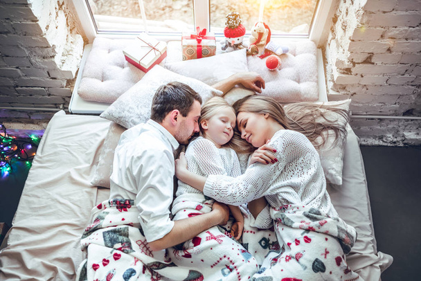 Happy family, mother, father and daughter resting on the white bed. Christmas decorations - Foto, Bild