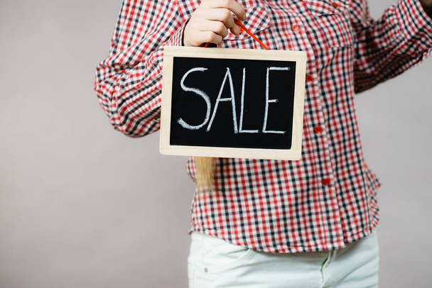 Unrecognizable woman wearing checked shirt holding sign banner with sale on black board. - 写真・画像