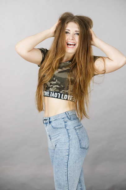 Beautiful young woman with long brown hair wearing stylish camo pattern tshirt and jeans making funny face. - Foto, immagini