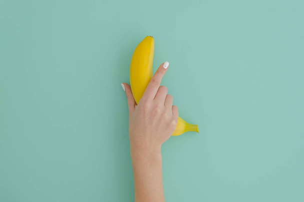 Female hand holding a banana on a mint tiffany background. Minimal fruit concept. - Photo, Image