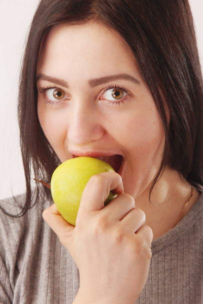 attractive girl with big beautiful eyes biting green apple - Zdjęcie, obraz