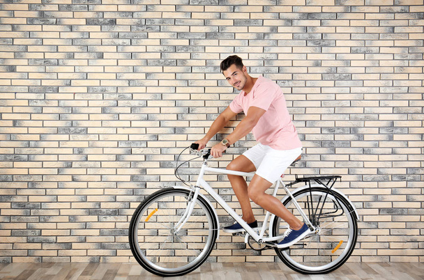 Handsome young hipster man riding bicycle near brick wall - Foto, Bild