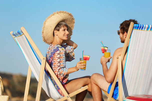 Young couple with cocktails in beach chairs at seacoast - 写真・画像