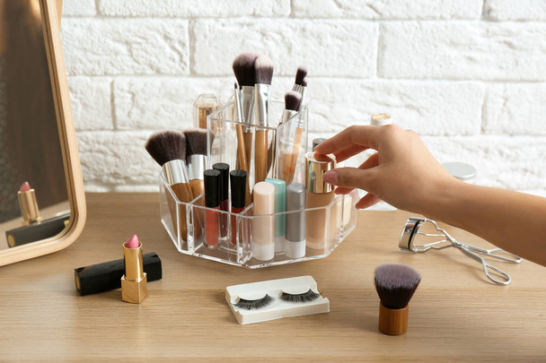 Woman taking cosmetics from organizer for makeup products on table - Photo, image