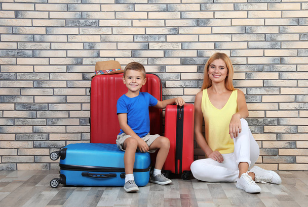Woman and her son with suitcases near brick wall. Vacation travel - Fotó, kép