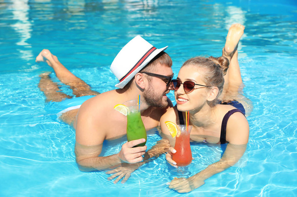 Young couple with refreshing cocktails in swimming pool at resort - Foto, imagen