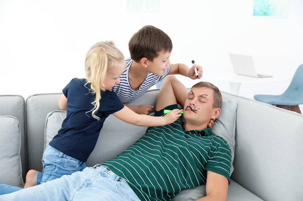 Маленькі діти малюють обличчя свого батька, коли він спить на дивані вдома. Квітневий день дурня
 - Фото, зображення