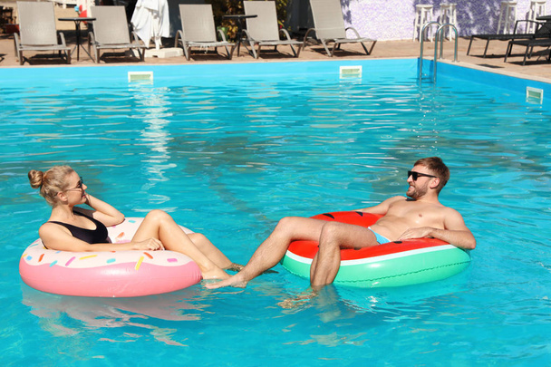 Happy young couple with inflatable rings in swimming pool - Photo, Image