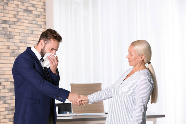 Mature woman handshaking with ill young man suffering from cough in office - Foto, Imagen
