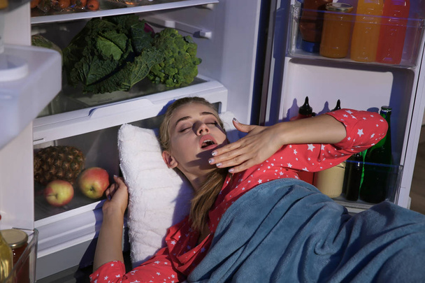 Young woman sleeping near refrigerator at night - Fotografie, Obrázek