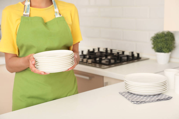 Woman holding stack of clean dishes in kitchen - Photo, image
