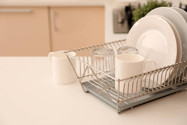 Dish drainer with clean dinnerware on table in kitchen. Space for text - Photo, image