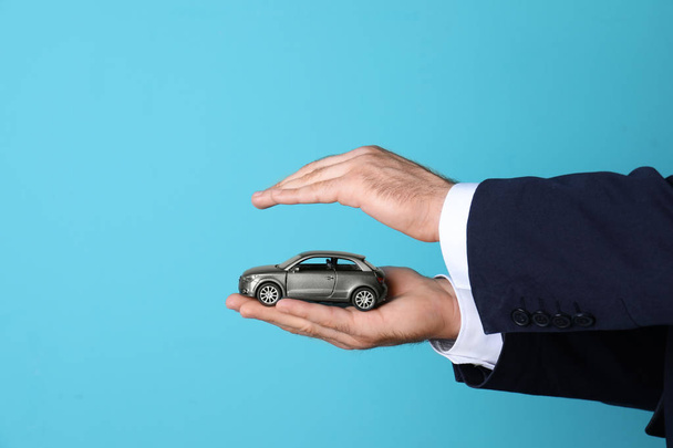 männlicher Versicherungsvertreter mit Spielzeugauto auf farbigem Hintergrund, Nahaufnahme. Raum für Text - Foto, Bild