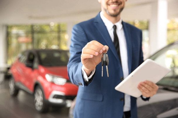 Salesman with car keys and tablet in auto dealership, closeup - Foto, afbeelding