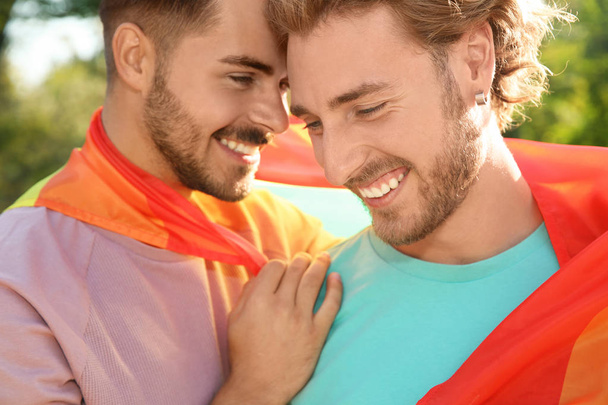 Happy gay couple with rainbow flag outdoors - Photo, image